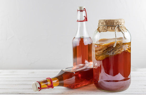 Kombucha in einem Glasgefäß mit SCOBY und zwei Flaschen fermentiertem Tee auf weißem Holztisch